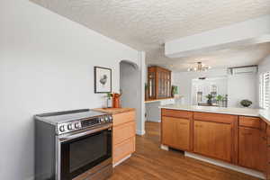 Kitchen with stainless steel electric stove, light countertops, dark wood-style flooring, glass fronted cabinets, and arched walkways