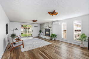 Living area featuring dark wood-style floors, a brick fireplace, and a textured ceiling