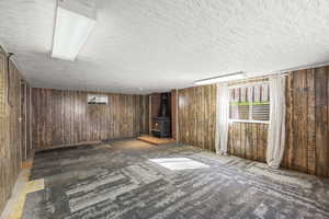Basement with wooden walls, a wood stove, and a textured ceiling