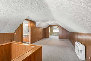 Additional living space with heating unit, carpet flooring, wood walls, and a textured ceiling