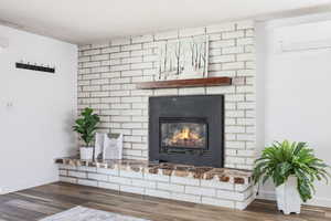 Detailed view of a mini split for heating / cooling, a brick fireplace, and wood finished floors