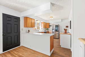 Kitchen featuring light countertops, wood finish cabinetry, a textured ceiling, stainless steel fridge, and light wood-style floors