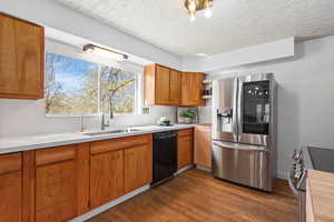 Kitchen with stainless steel appliances, light countertops, wood finish cabinetry, and a textured ceiling