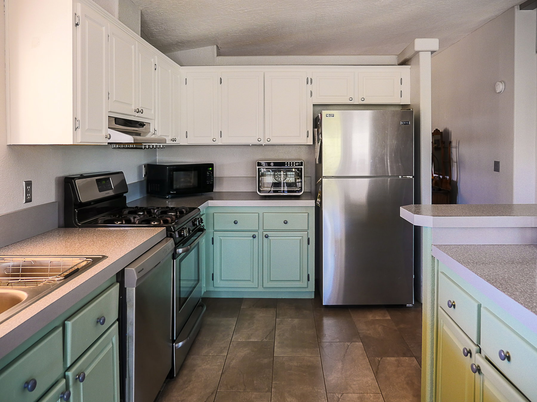 Kitchen with two tone cabinetry, stainless steel appliances, light countertops, ventilation hood, and a textured ceiling