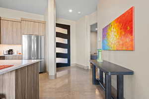 Kitchen featuring modern cabinets, freestanding refrigerator, light wood finish cabinetry, finished concrete flooring, and light stone countertops