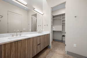 Bathroom featuring double vanity, concrete floors, and a walk in closet