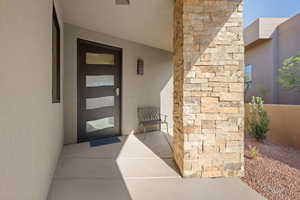 Doorway to property with stucco siding, stone siding, and a patio