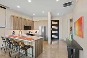 Kitchen with a peninsula, a breakfast bar area, modern cabinets, stainless steel appliances, and light wood finish cabinets