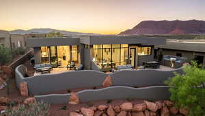 Back of property at dusk featuring a mountain view, a patio, stucco siding, and an outdoor living / dining area