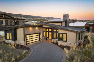 View of front facade featuring stone siding, driveway, a garage, and a chimney