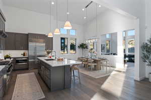 Kitchen with a high ceiling, a center island with sink, light stone countertops, decorative light fixtures, and premium appliances