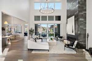 Living area with a premium fireplace, dark wood-style floors, healthy amount of natural light, a chandelier, and a high ceiling