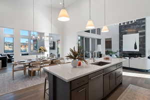 Kitchen with open floor plan, light stone countertops, dark wood-style floors, stainless steel dishwasher, and a high ceiling