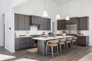 Kitchen featuring dark wood finish cabinetry, hanging light fixtures, a center island with sink, a breakfast bar area, and high end appliances