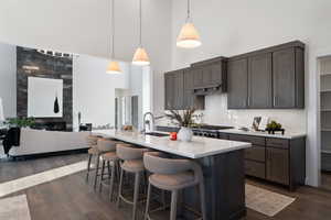 Kitchen with a high ceiling, open floor plan, dark wood-style floors, light stone counters, and a kitchen breakfast bar