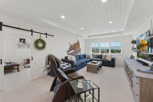 Living area with a barn door, a wooden tray ceiling, recessed lighting, and light colored carpet