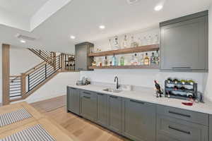 Indoor wet bar featuring open shelves, gray cabinets, light wood-style flooring, light stone countertops, and recessed lighting
