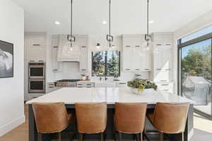 Kitchen featuring stainless steel appliances, decorative light fixtures, light stone counters, a center island, and light wood-style floors