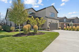 Modern inspired farmhouse with a garage, driveway, a front lawn, and board and batten siding