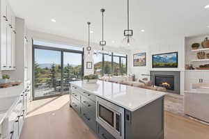 Kitchen with light wood finished floors, stainless steel microwave, a kitchen island, open floor plan, and light stone counters