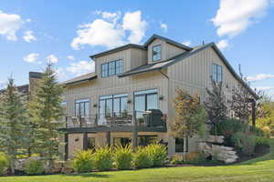Back of house featuring board and batten siding, a lawn, a balcony, roof with shingles, and a chimney