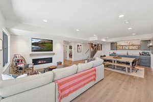 Living room with light wood finished floors, a lit fireplace, recessed lighting, bar, and wooden walls