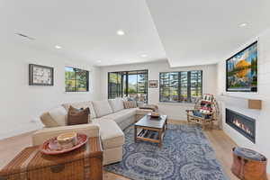 Living area with a glass covered fireplace, wood finished floors, and recessed lighting