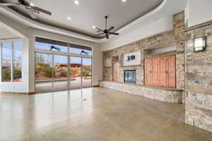 Unfurnished living room featuring a fireplace, ceiling fan, and a tray ceiling
