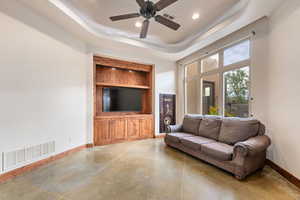 Living area with finished concrete floors, a tray ceiling, a ceiling fan, recessed lighting, and built in features