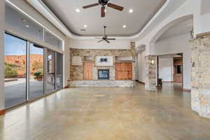 Unfurnished living room featuring concrete flooring, a mountain view, ceiling fan, a fireplace, and a tray ceiling