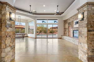 Unfurnished living room with a tray ceiling, a fireplace, arched walkways, and a ceiling fan
