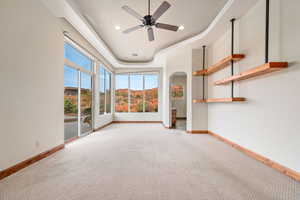 Unfurnished room featuring a raised ceiling, a ceiling fan, recessed lighting, arched walkways, and light carpet