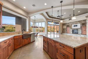 Kitchen with wood finish cabinetry, light stone counters, concrete flooring, ceiling fan, and a fireplace