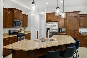 Kitchen with stainless steel appliances, light stone countertops, a breakfast bar area, and a kitchen island with sink