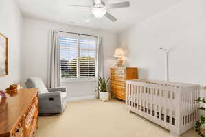 Bedroom with light carpet, a crib, and a ceiling fan
