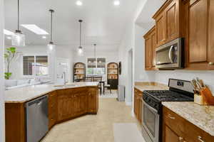 Kitchen with stainless steel appliances, wood finish cabinets, light stone counters, a skylight, and hanging light fixtures