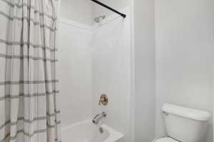 Full bathroom with toilet and shower / bath combination with curtain