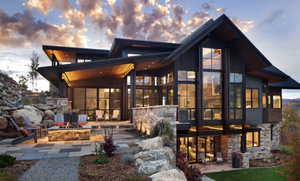 Back of house at dusk with a patio area, an outdoor fire pit, and stone siding
