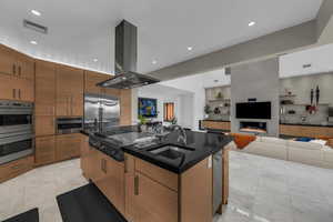 Kitchen with open floor plan, island exhaust hood, stainless steel appliances, an island with sink, and dark stone counters