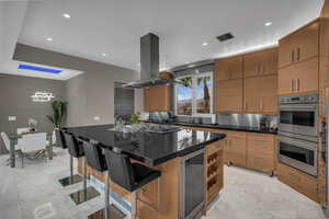 Kitchen with a center island with sink, a kitchen breakfast bar, dark stone counters, stainless steel double oven, and wine cooler