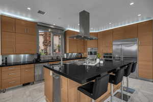 Kitchen with an island with sink, a breakfast bar, stainless steel appliances, island exhaust hood, and wood finish cabinetry