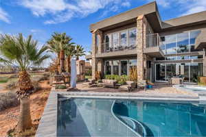 Back of house featuring a balcony, a patio, an in-ground hot tub, an outdoor pool, and stone siding