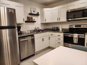 Kitchen featuring stainless steel appliances, white cabinetry, open shelves, and dark stone counters