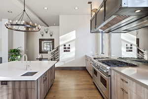 Kitchen with ventilation hood, range with two ovens, light stone countertops, dark wood finished floors, and a kitchen island with sink