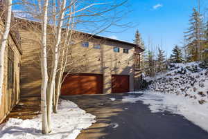 View of snowy exterior with asphalt driveway and an attached garage