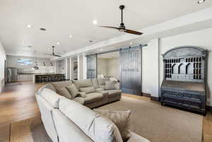 Living area featuring a barn door, ceiling fan, recessed lighting, wood finished floors, and bar area
