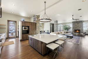 Kitchen with a chandelier, an island with sink, a breakfast bar, dark wood finished floors, and recessed lighting