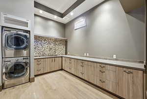 Laundry area with stacked washing machine and dryer, light wood-type flooring, and recessed lighting