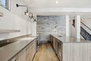 Kitchen with light wood finished floors, dark stone counters, stainless steel electric range, an accent wall, and beverage cooler