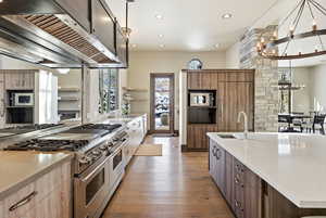 Kitchen featuring premium range hood, stainless steel appliances, light stone counters, a chandelier, and light wood finished floors